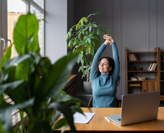 Frau dehnt während sie am Schreibtisch sitzt